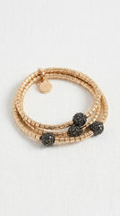 Envy gold beaded wrap bracelet with three textured black crystal ball charms, displayed on a light off-white fabric background.