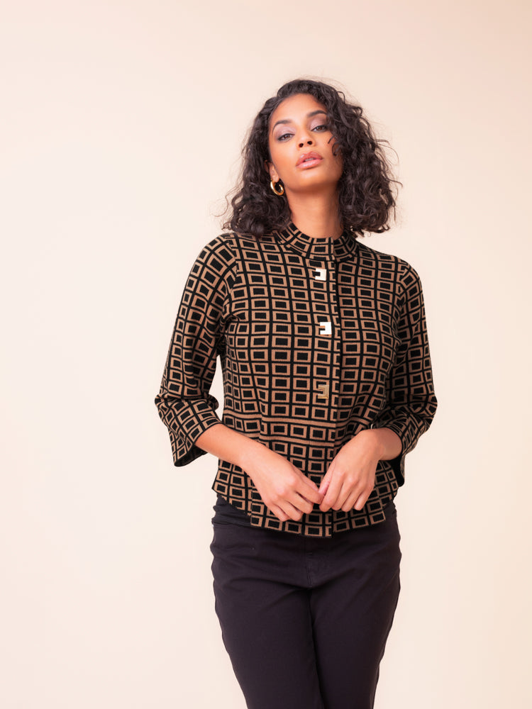 A woman modeling a black and brown geometric patterned blouse with three-quarter sleeves and a high mock neck, paired with black pants, against a solid light beige background.