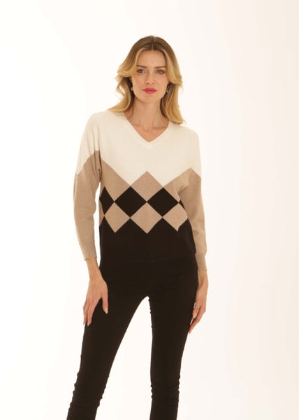 A woman modeling a long-sleeve V-neck sweater with a color-blocked argyle pattern in cream, beige, black, and brown, paired with black pants against a plain white background.