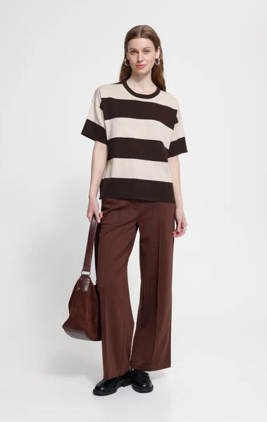 A woman stands against a light grey studio background wearing a short sleeve Ichi top with wide horizontal brown and cream stripes.