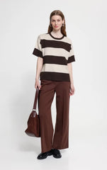 A woman stands against a light grey studio background wearing a short sleeve Ichi top with wide horizontal brown and cream stripes.