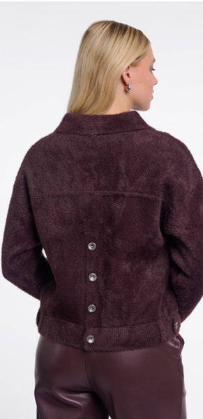 A woman shown from the back wearing a dark plum-brown Rino Pelle textured jacket with a button closure down the back, paired with matching dark pants, against a plain white background.