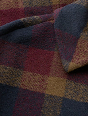 A close-up of a textured plaid fabric with a checkered pattern in navy blue, burgundy red, and mustard yellow.