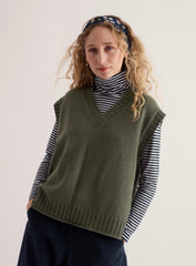 A woman wearing Seasalt olive green knit vest over a black and white striped turtleneck, paired with dark navy pants and a navy patterned headband, photographed against a plain light background.