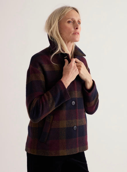 A woman wearing a Seasalt dark wool-blend jacket with burgundy, navy, and brown tones, standing against a plain light background.