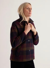 A woman wearing a Seasalt dark wool-blend jacket with burgundy, navy, and brown tones, standing against a plain light background.