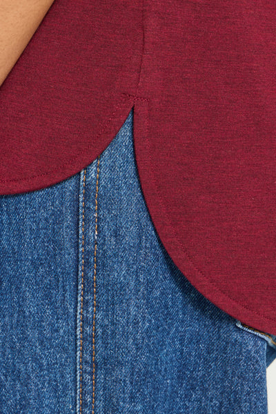 Close-up detail of a heathered burgundy top with a scalloped or curved hem layered over blue denim jeans.