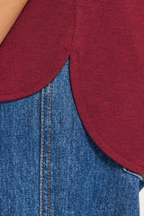Close-up detail of a heathered burgundy top with a scalloped or curved hem layered over blue denim jeans.