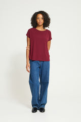 A woman modeling a short-sleeve crewneck t-shirt in burgundy and wide-leg blue jeans, standing against a plain white studio background.
