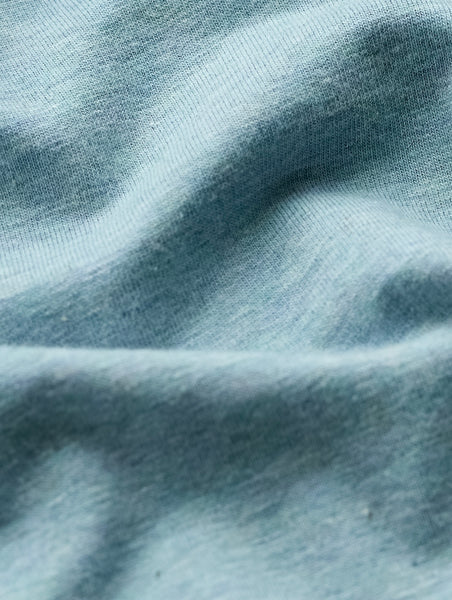 A close-up of light blue knit fabric with soft folds and a fine ribbed texture.