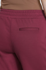 Close-up of a person wearing burgundy  pants with an elastic waistband and a welt pocket, paired with a tan top.