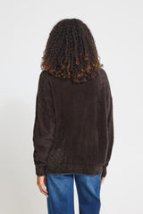 A person shown from the back wearing a Ichi dark brown  long-sleeve cardigan and blue jeans against a plain light grey studio background.