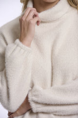 Close up of a person wearing Rino & Pelle cream coloured knit turtleneck sweater against a plain light background.