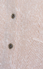 Close-up of a textured cream-colored knit fabric with two dark metal buttons.