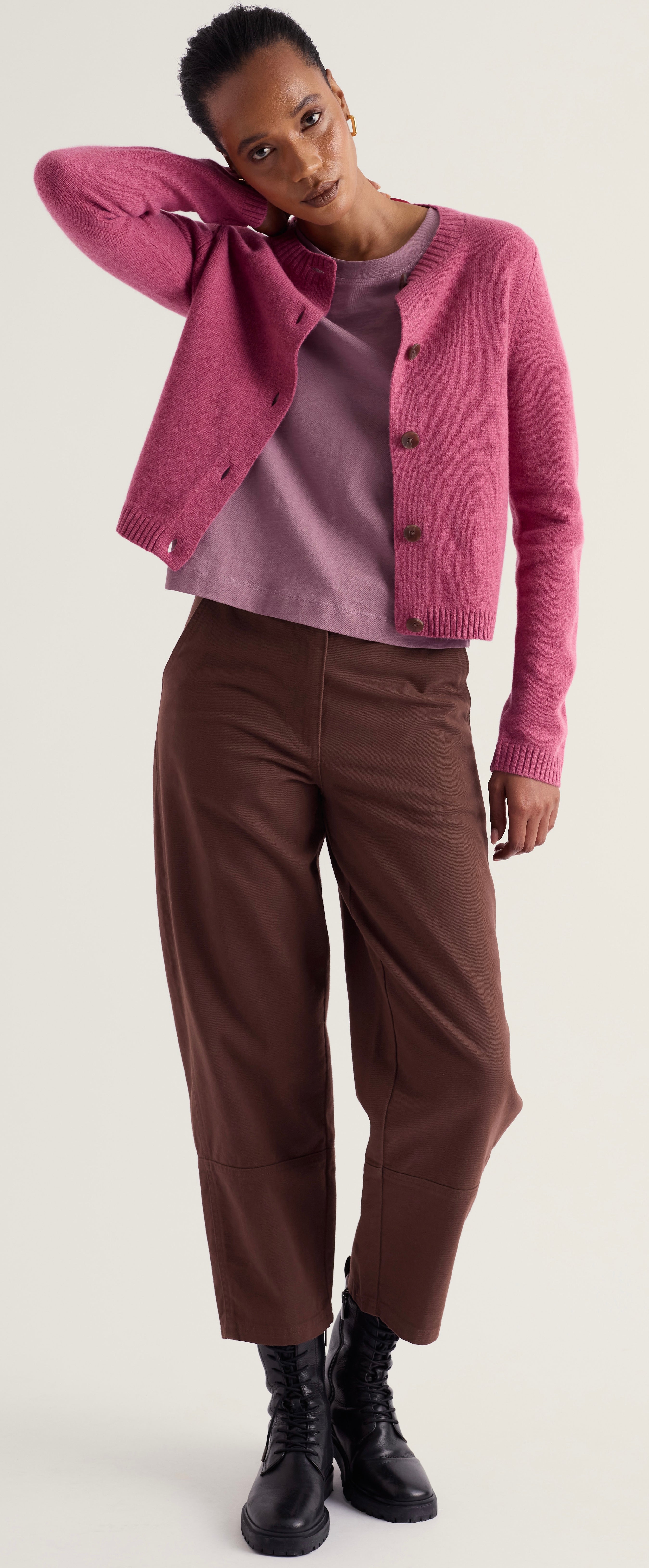 A model wearing Seasalt dusty pink cropped cardigan over a mauve top, paired with brown cropped trousers and black lace-up ankle boots, against a light gray studio background.