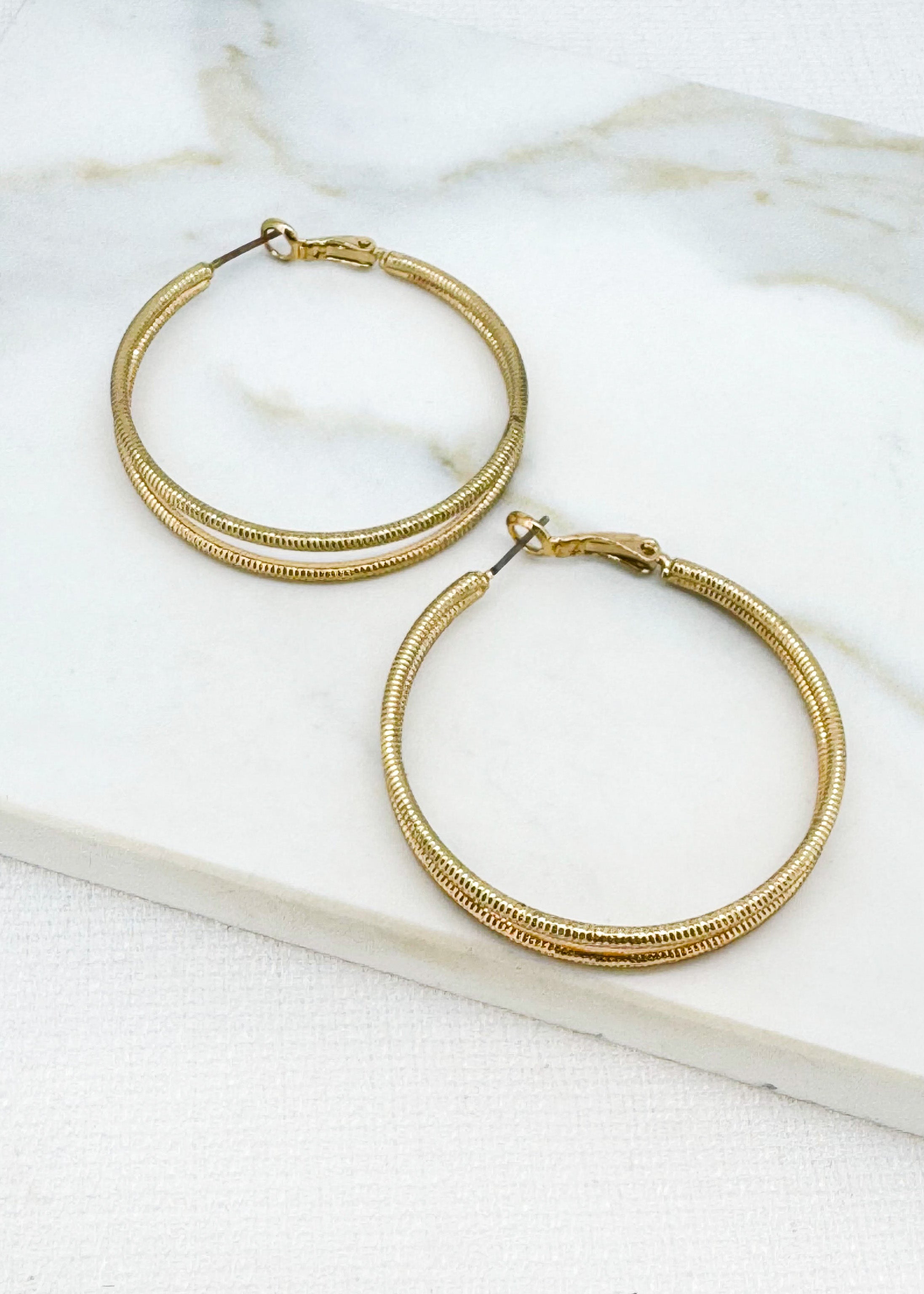 Envy Jewellery large Gold hoop earrings on a marble surface.