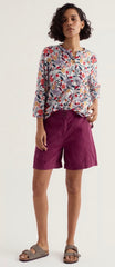 Woman wearing a floral blouse and purple shorts on a white background