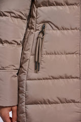 Close-up of a padded coat in a taupe-beige colour showing horizontal stitching, a vertical zippered pocket with a matching zipper pull, and a hand at the bottom left.