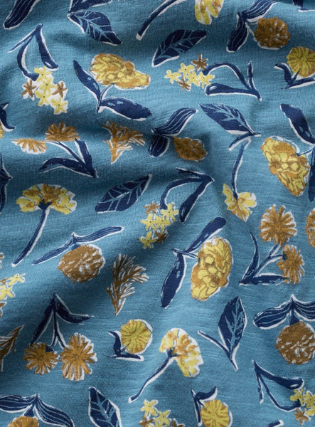 A close up of a blue fabric with a repeating floral pattern in yellow and navy blue.