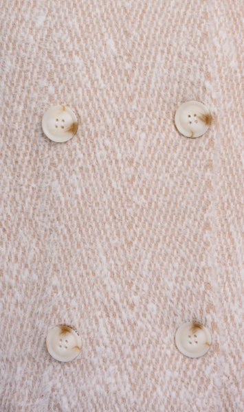 Close up of a textured cream coloured woven fabric with four off-white buttons arranged in a grid.