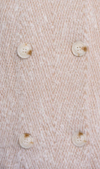 Close up of a textured cream coloured woven fabric with four off-white buttons arranged in a grid.