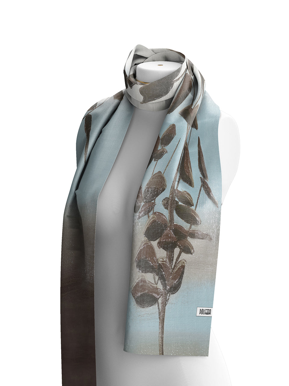 Dolcezza lightweight rectangular scarf draped on a white mannequin torso against a plain white background. The scarf features a botanical print with brown seed pods on a light blue and gray base, with a darker gray-to-brown gradient along one edge.