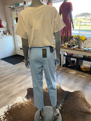 Mannequin wearing a light-colored shirt and blue pants in a room with furniture and decor.