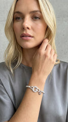 Woman wearing a grey top modelling an Envy silver beaded bracelet with a G diamanté pendant. Against a studio backdrop.
