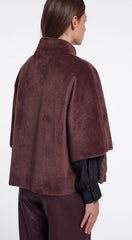 A woman shown from the back wearing a dark brown plush faux fur cape  over a black long sleeve top and matching brown pants, against a plain white studio background.