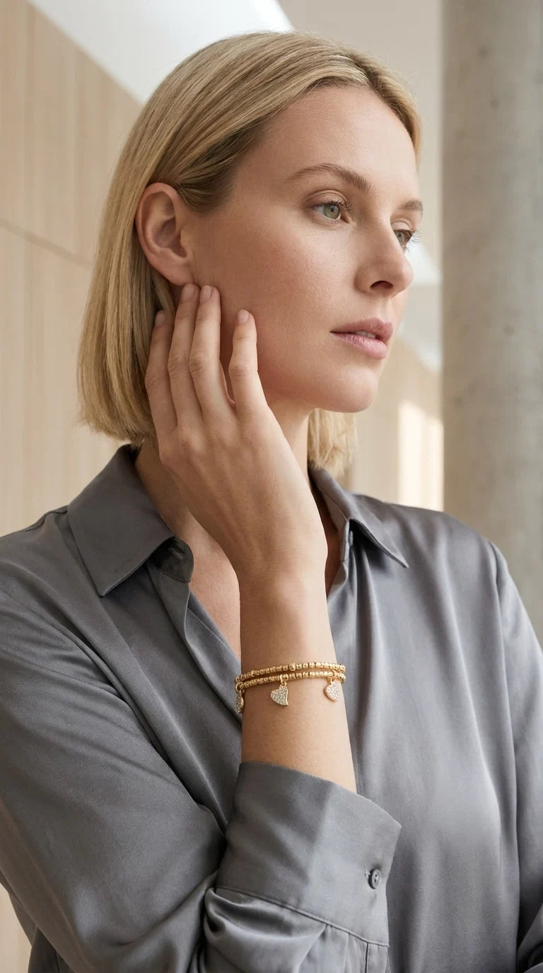Women wearing a grey blouse modelling an Envy gold wraparound bracelet with heart and circle diamanté charms. Against a studio background.