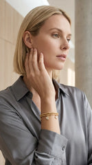 Women wearing a grey blouse modelling an Envy gold wraparound bracelet with heart and circle diamanté charms. Against a studio background.