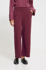 A person wearing Ichi wide-leg trousers in a deep burgundy/maroon colour, paired with a matching burgundy and white striped shirt and black loafers, against a plain white studio background.