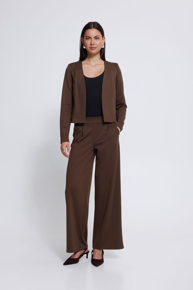 A woman modelling a matching brown two-piece suit consisting of a cropped open-front jacket and Ichi wide leg trousers, styled with a black top and dark brown pointed-toe heels against a light grey  studio background.