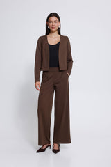 A woman modelling a matching brown two-piece suit consisting of a cropped open-front jacket and Ichi wide leg trousers, styled with a black top and dark brown pointed-toe heels against a light grey  studio background.