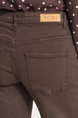Close-up of the back waistband and back pocket of dark brown denim jeans, showing a tan leather patch with the brand name 'ICHI'.