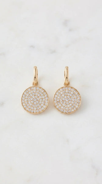 Envy pair of gold drop earrings with round pave diamond disc charms, displayed on a light marble surface.