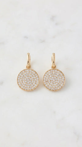 Envy pair of gold drop earrings with round pave diamond disc charms, displayed on a light marble surface.