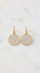 Envy pair of gold drop earrings with round pave diamond disc charms, displayed on a light marble surface.