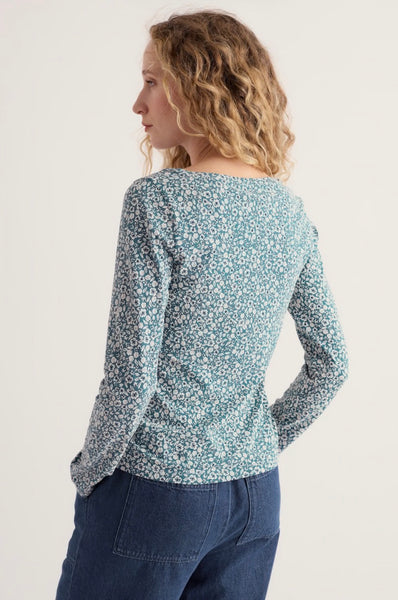 A woman is shown from the back wearing a Seasalt a long sleeve top with a dense blue and white floral pattern, paired with dark blue jeans, against a plain light background.
