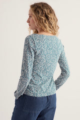 A woman is shown from the back wearing a Seasalt a long sleeve top with a dense blue and white floral pattern, paired with dark blue jeans, against a plain light background.