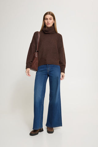 A woman with long light brown hair wearing a Ichi dark brown ribbed knit turtleneck sweater against a light grey studio background.