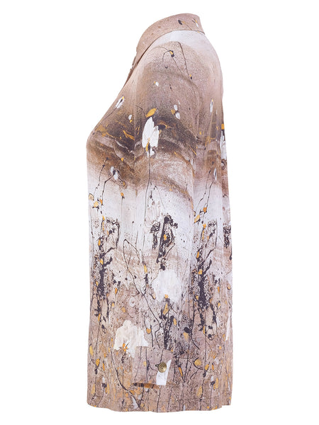 A side-profile view of a women's Dolcezza long-sleeve collared shirt featuring an abstract paint-splatter print in beige, brown, white, and black with small yellow accents, set against a plain white background.