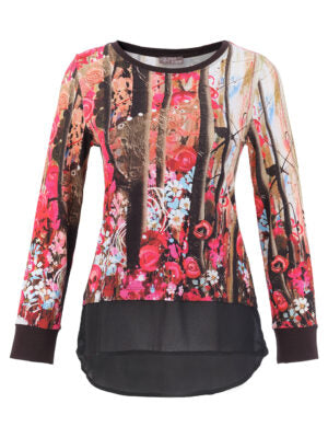 A long-sleeve Dolcezza top featuring a vibrant pink, red, and blue floral print on one side, transitioning into a black and brown vertical tree trunk pattern on the other, finished with a solid black ruffled hem and cuffs.