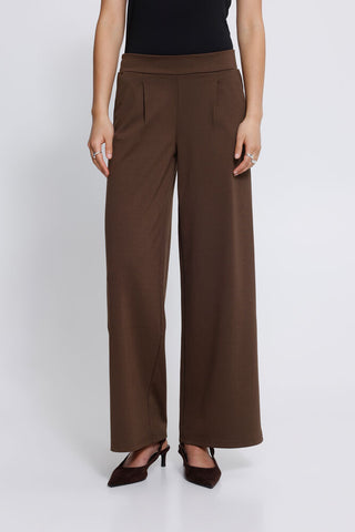 Close up of a person wearing brown wide leg trousers, showing the back waistband, a side welt pocket, and the side of the leg against a light grey studio background.