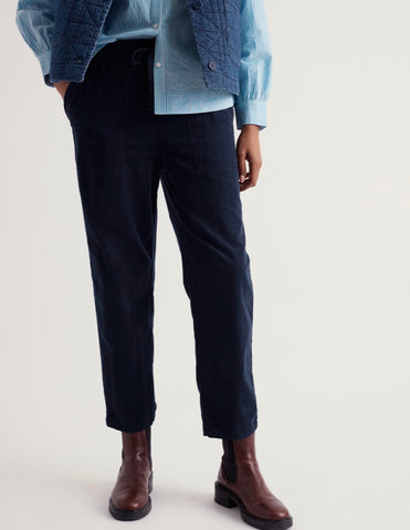 A pair of dark navy blue trousers with an elastic waistband and drawstring, displayed flat against a light beige background.