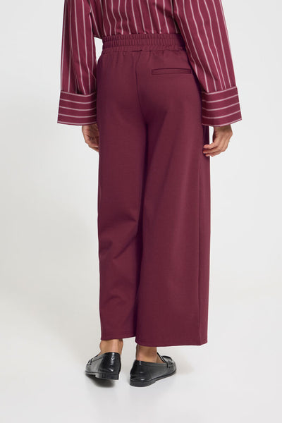 Person wearing a maroon striped shirt and wide-leg pants on a white background