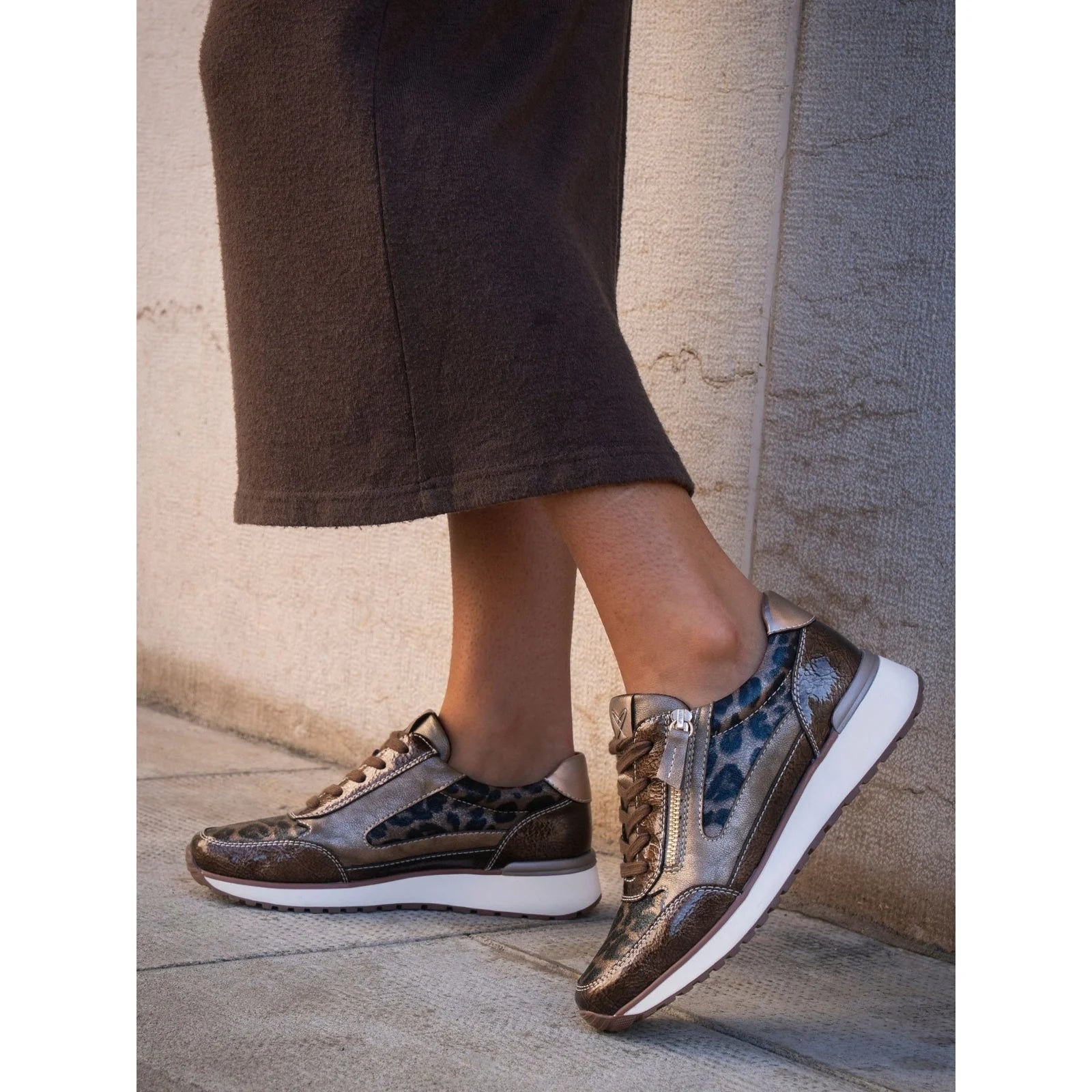 Person wearing patterned Lunar sneakers on a stone pavement with a neutral wall background
