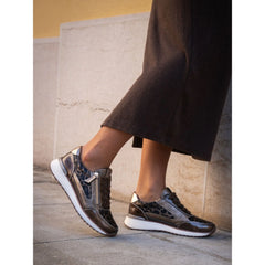 Person wearing metallic sneakers on a stone pavement with a neutral wall background