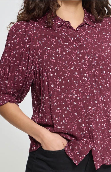 Women wearing an Ichi button shirt in floral print with hand in pocket of black trousers against a studio light grey background.