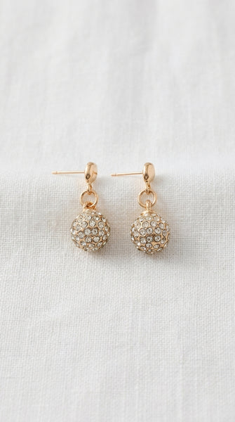 Envy Jewellery a pair of gold-toned dangle earrings with round, crystal-encrusted balls, displayed on a textured white fabric background.